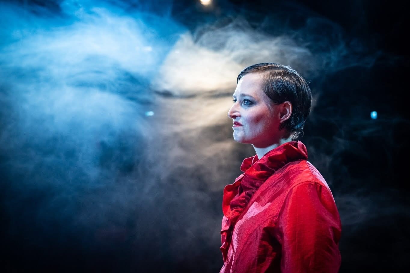 Gaby in profile in a red ruffled blouse against blue haze.