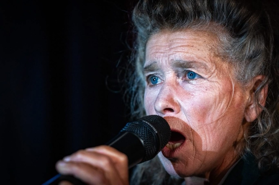 Mamy sings into a microphone in extreme close-up.