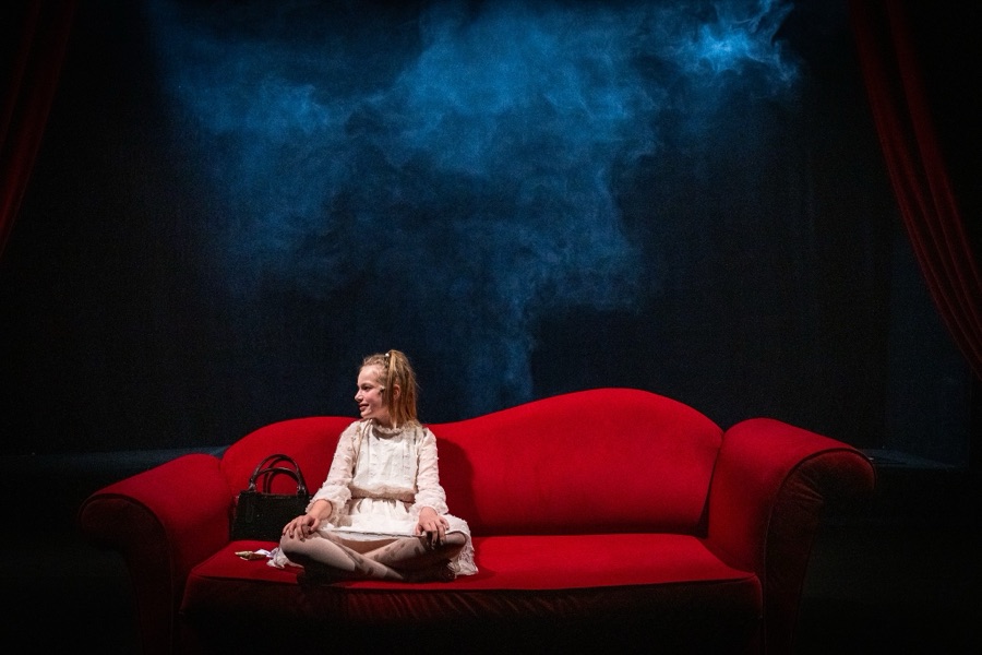 Catherine sits cross-legged on the red sofa under a cloud of blue haze.