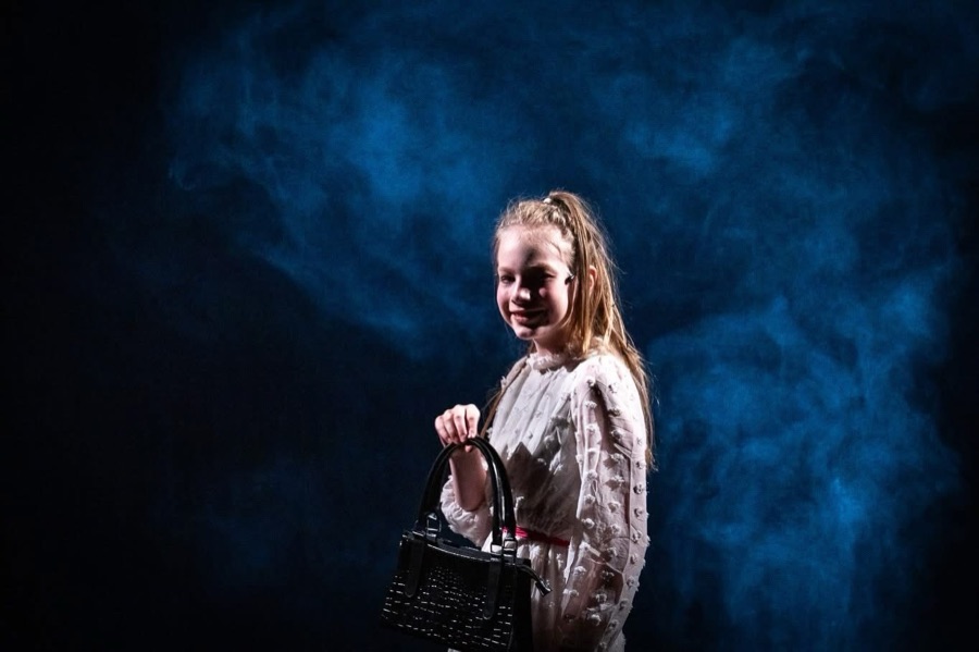 Catherine, with a black handbag, smiles at the audience against blue haze.
