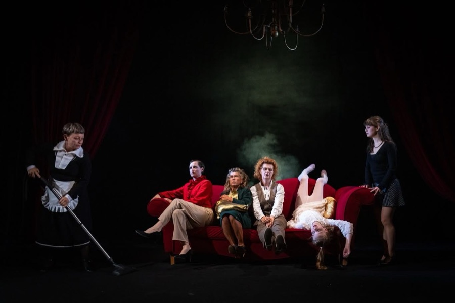 The household gathered around the red sofa while the maid vacuums; Catherine hangs upside down.