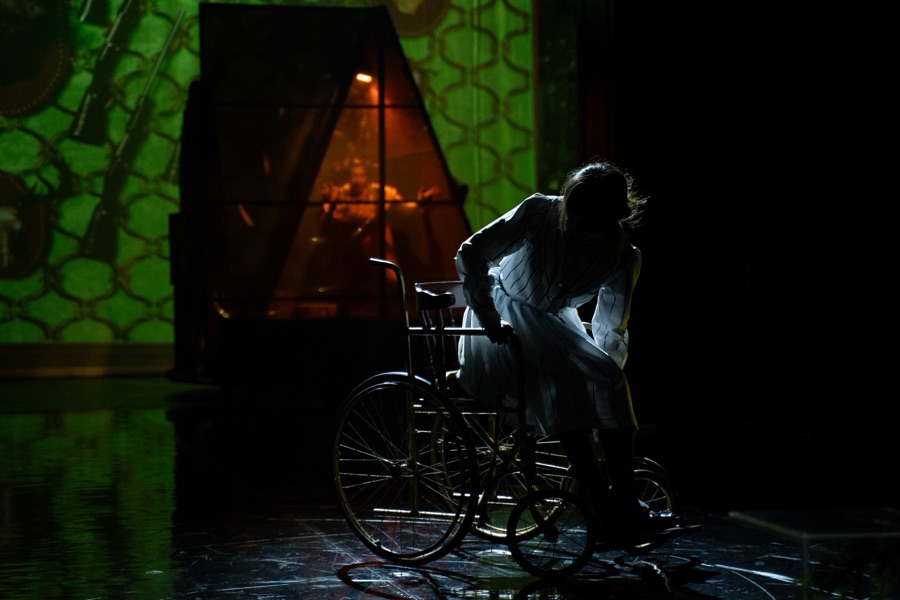 Klara rises from her wheelchair in front of the glowing doorway.