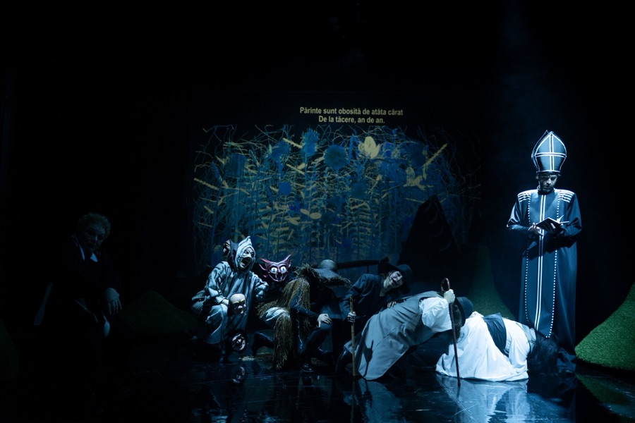 The priest in white stands over the kneeling villagers in deep blue light.
