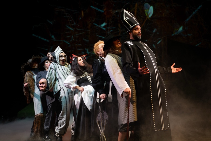 The villagers in masks and hats crowd behind the priest in a tall mitre.