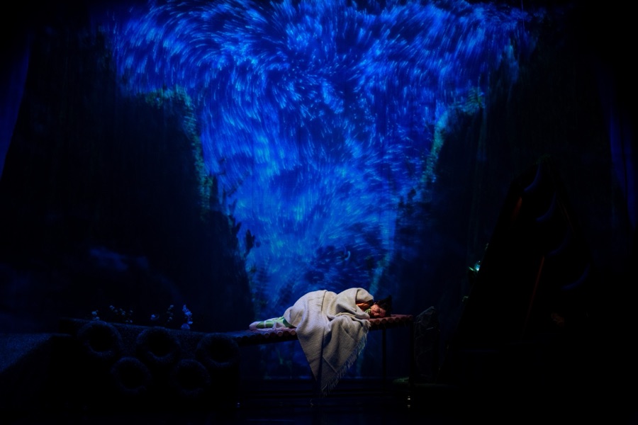 Heidi asleep on a raised bed under a swirling blue projection.