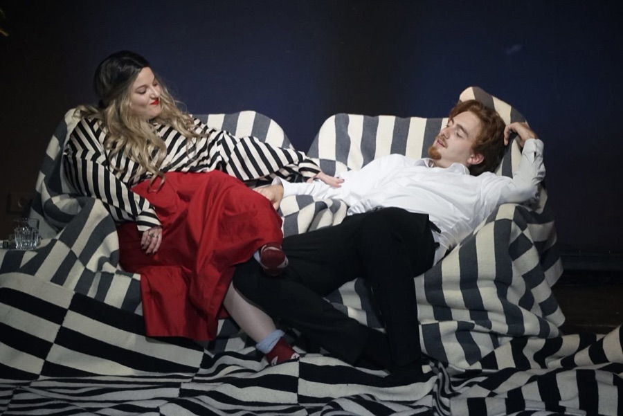 The couple stretched out on a sofa draped in black and white stripes, she in a striped blouse and red skirt, he in a white shirt.