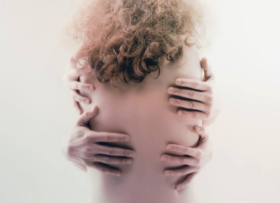Several pairs of hands embrace a bare back below a head of curly hair.