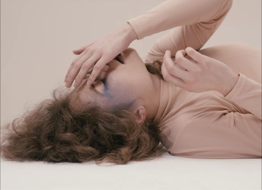 She covers her eyes with one hand, lying on the pale floor.