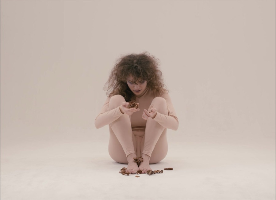 She sits folded up on the white floor, leaves scattered at her feet.