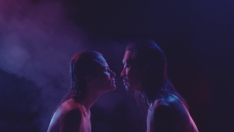 The two dancers face each other, almost touching, in violet haze.