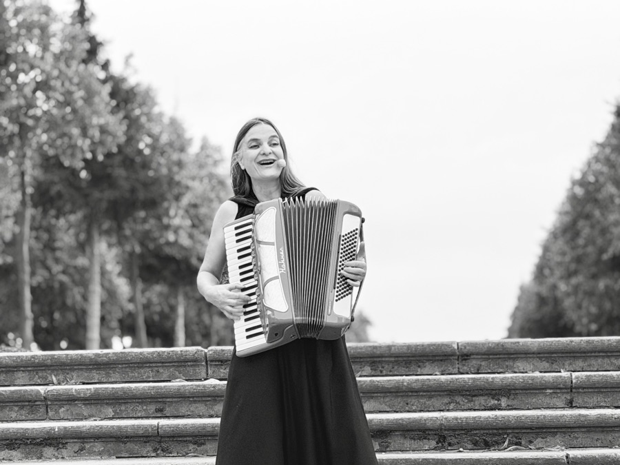 Black-and-white photo of AnniKa von Trier singing and playing the accordion on the garden steps at Rheinsberg.