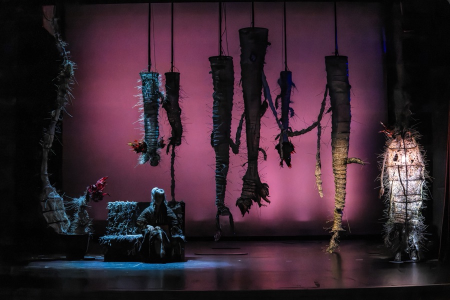 The full set against a pink backdrop: hanging thorny forms, the sofa and a glowing cocoon.