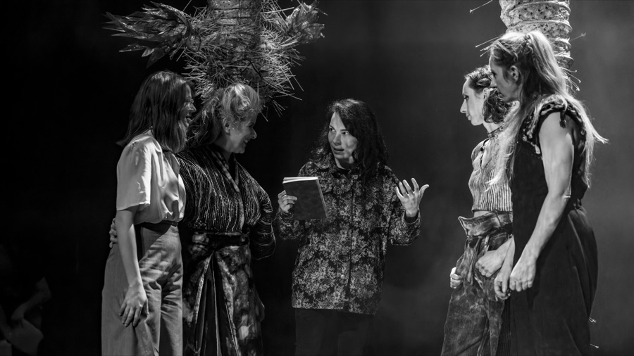 Black and white rehearsal photo: Petra Rațiu, notebook in hand, talks with the three actresses on the set.