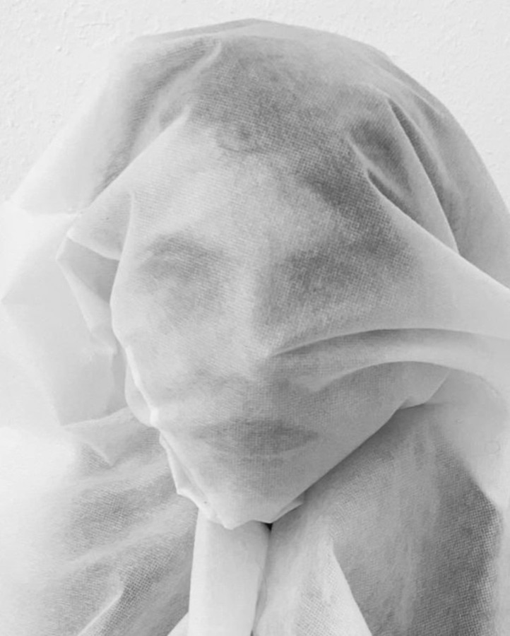 Black and white close-up of a face veiled in translucent white fabric.