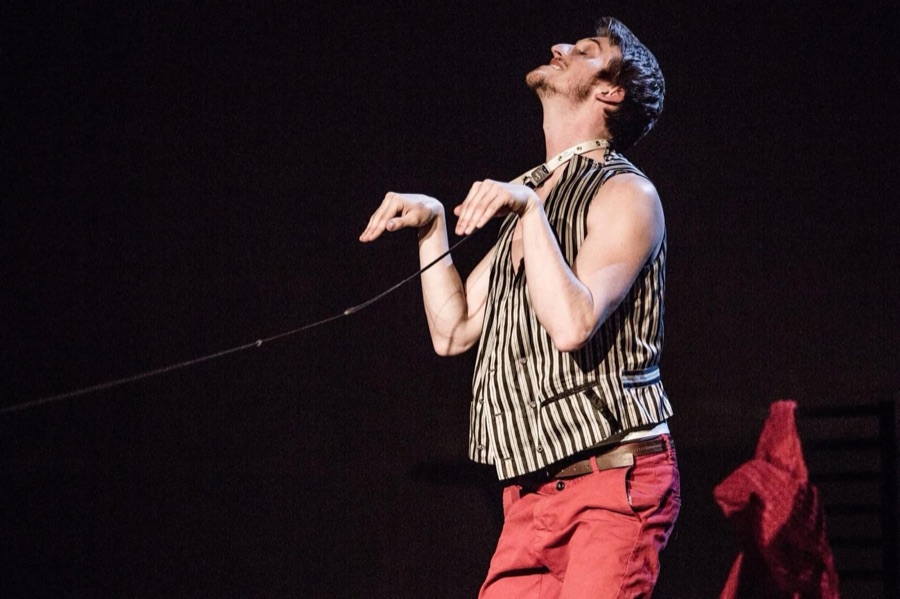 The man in a striped waistcoat leans back, held on a leash that stretches out of the frame.