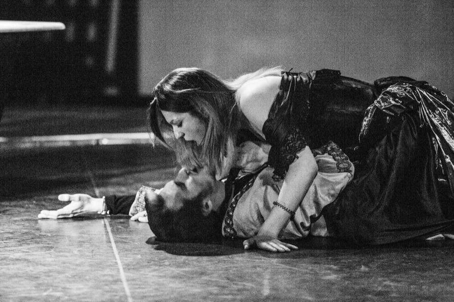 Black and white: she leans over him as he lies on the stage floor.