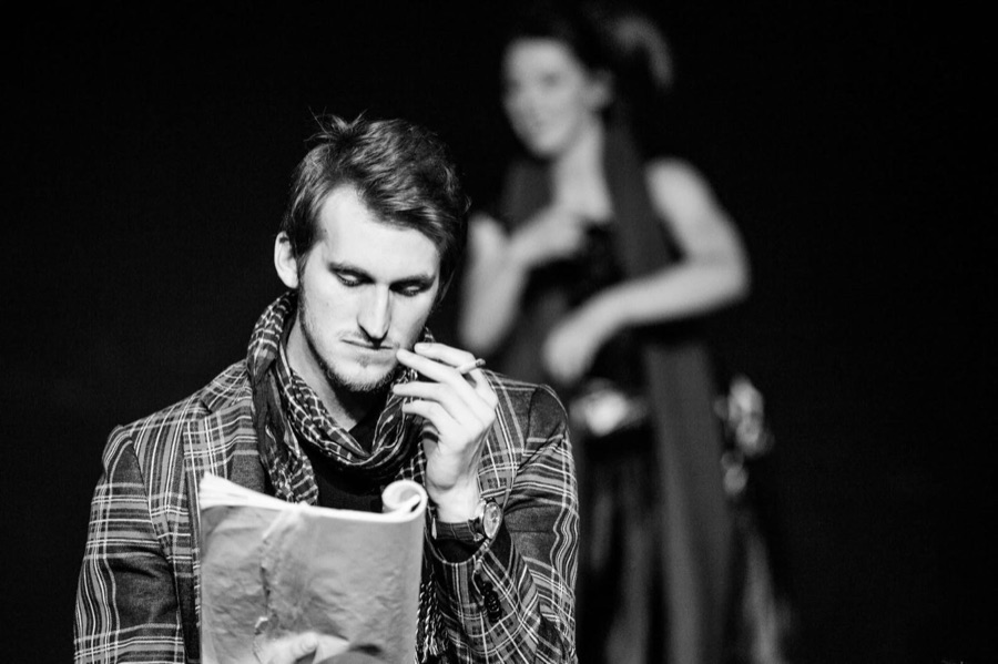 Black and white: the man reads from a script in the foreground, the woman out of focus behind him.